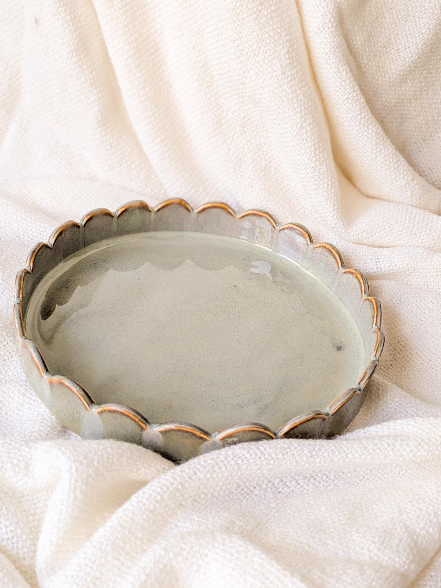 Scalloped ceramic plate with a opal green glaze and a golden brown rim.